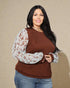 Woman wearing a brown top with floral sleeves against a beige background