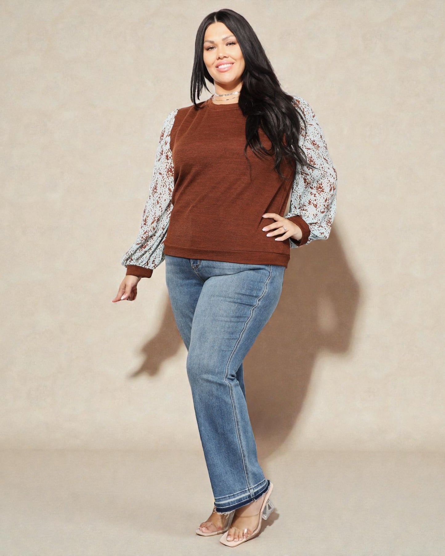 Woman wearing a brown top and blue jeans against a beige background