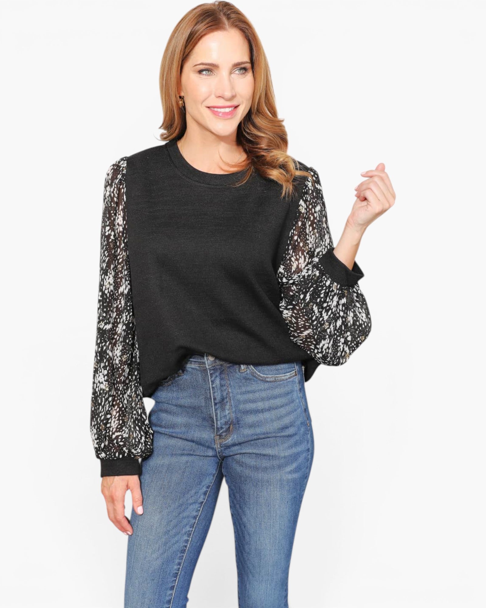 A woman modeling a black crewneck sweater with long, sheer patterned sleeves in black and white, paired with blue jeans against a plain white background.