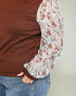 Close-up of a person wearing a brown top with floral sleeves against a neutral background