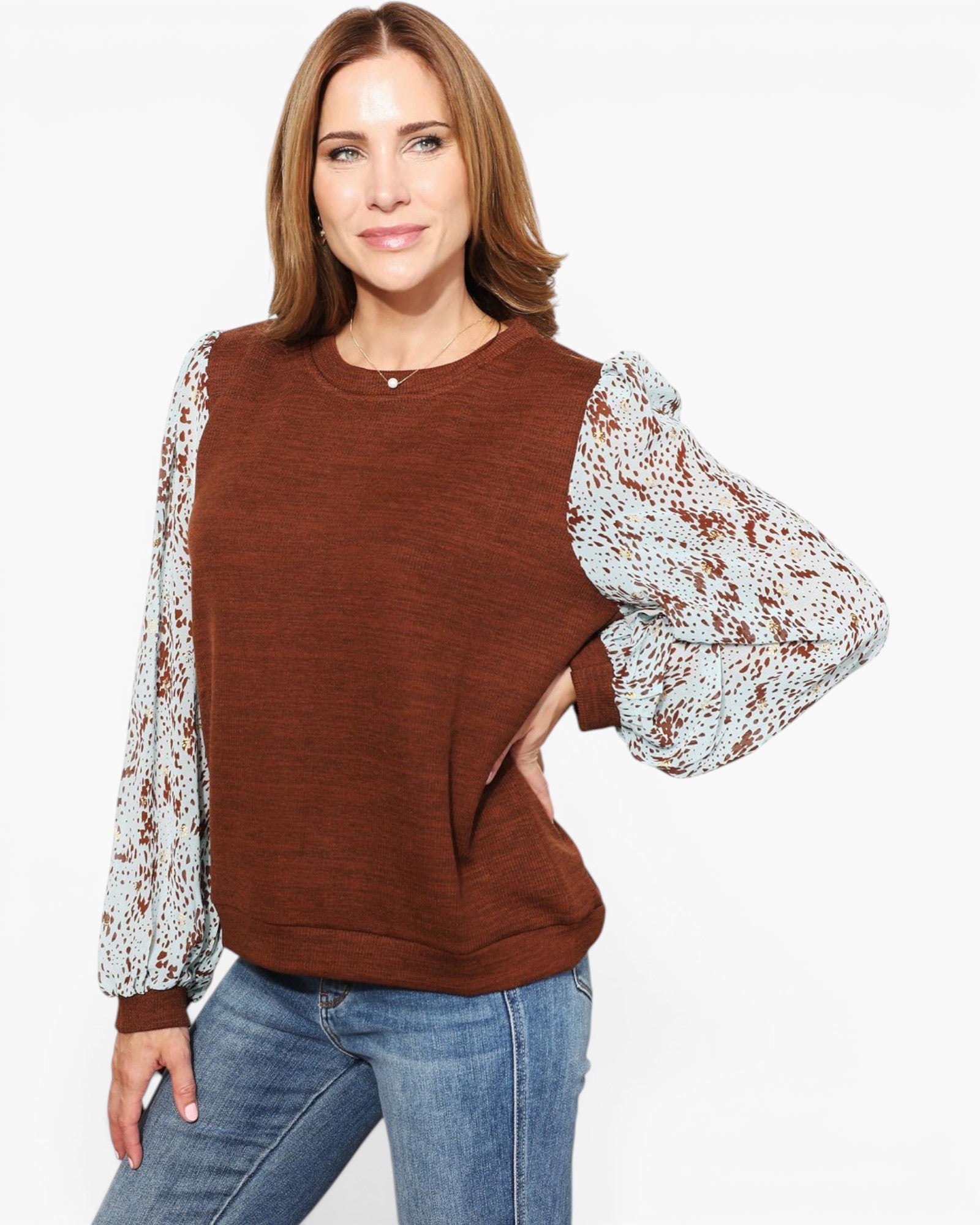 A woman modeling a brown crewneck sweatshirt with textured, patterned balloon sleeves in white and brown, paired with blue jeans against a plain white background.