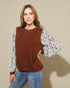 Woman wearing a brown sweater with floral sleeves against a beige background