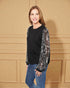 Woman wearing a black sweater with sheer sleeves against a beige wall