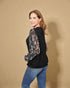 Woman wearing a black top with sequin sleeves against a beige background
