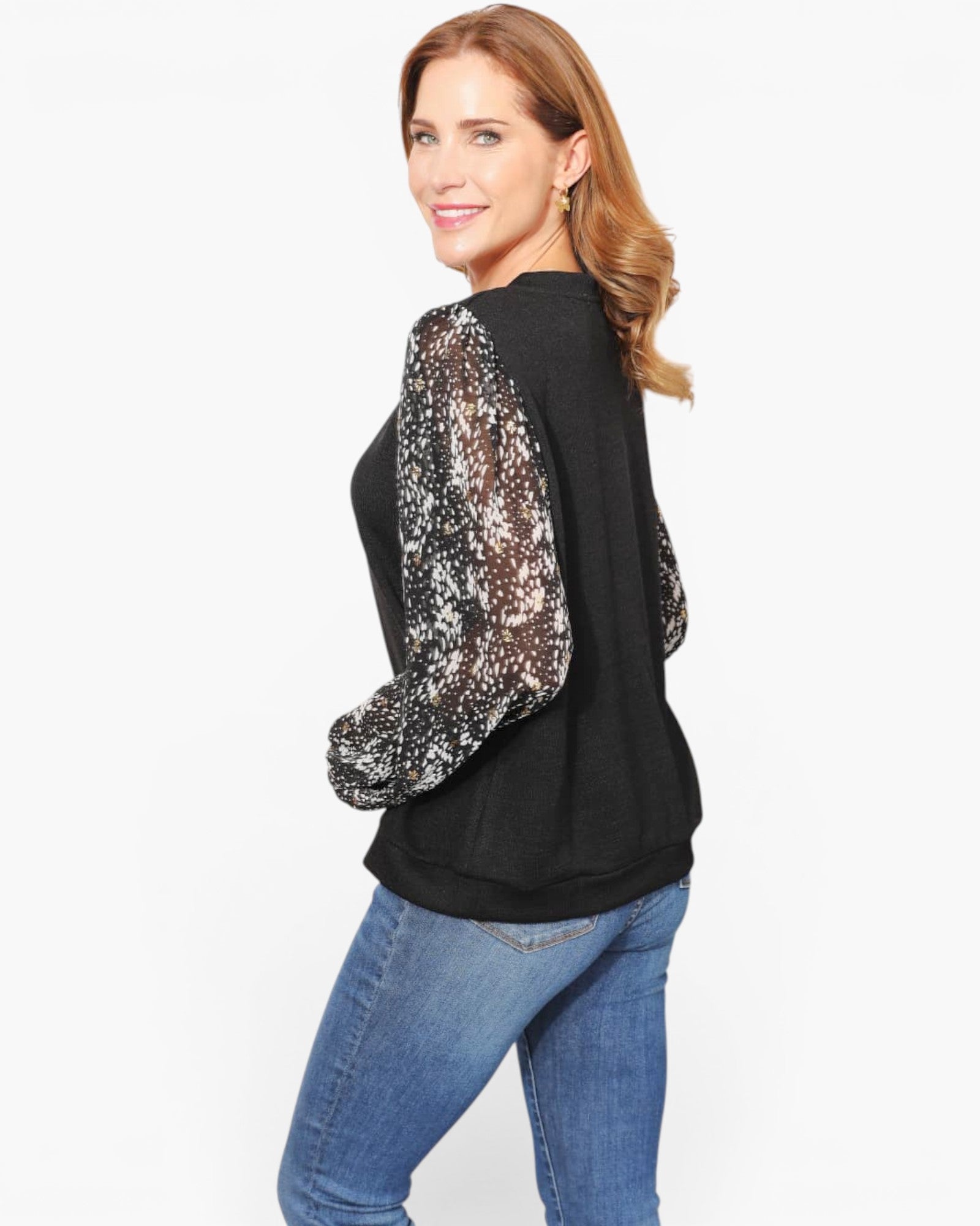 A woman modeling a black long-sleeve top with sheer, sequined puff sleeves, paired with blue jeans, against a plain white studio background.