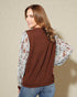 Woman wearing a brown vest over a floral shirt with a beige background