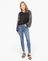 A woman modeling a black long-sleeve top with sheer patterned sleeves, paired with blue skinny jeans and black heeled sandals, against a plain white studio background.