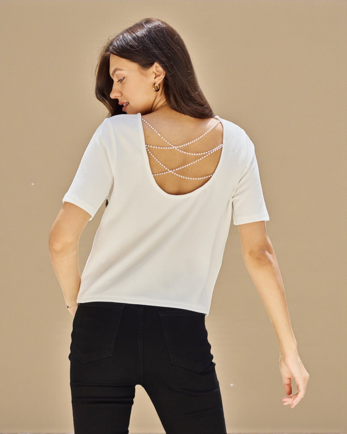 Woman wearing a white top with a decorative back design on a beige background