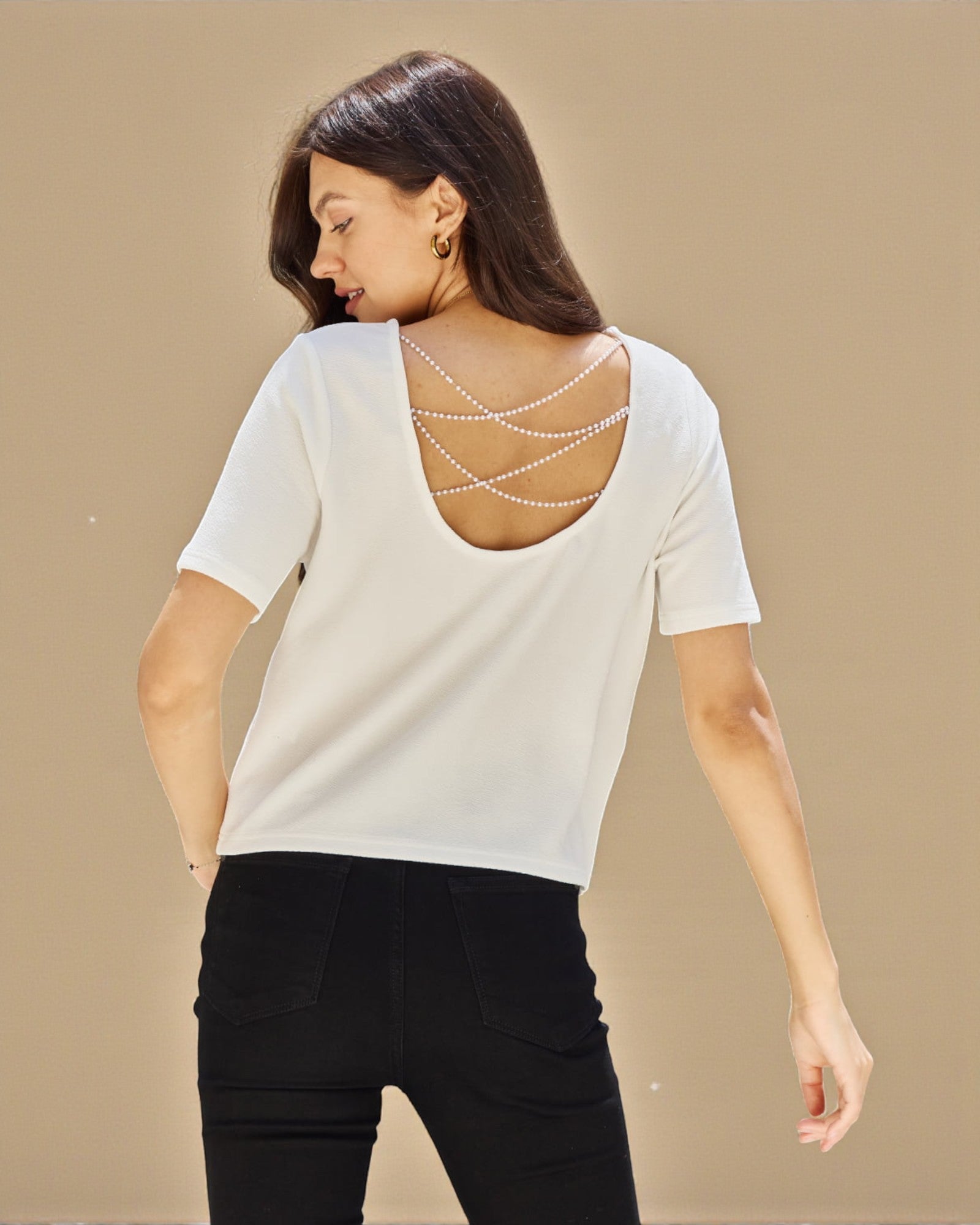 Woman wearing a white top with a decorative back design on a beige background