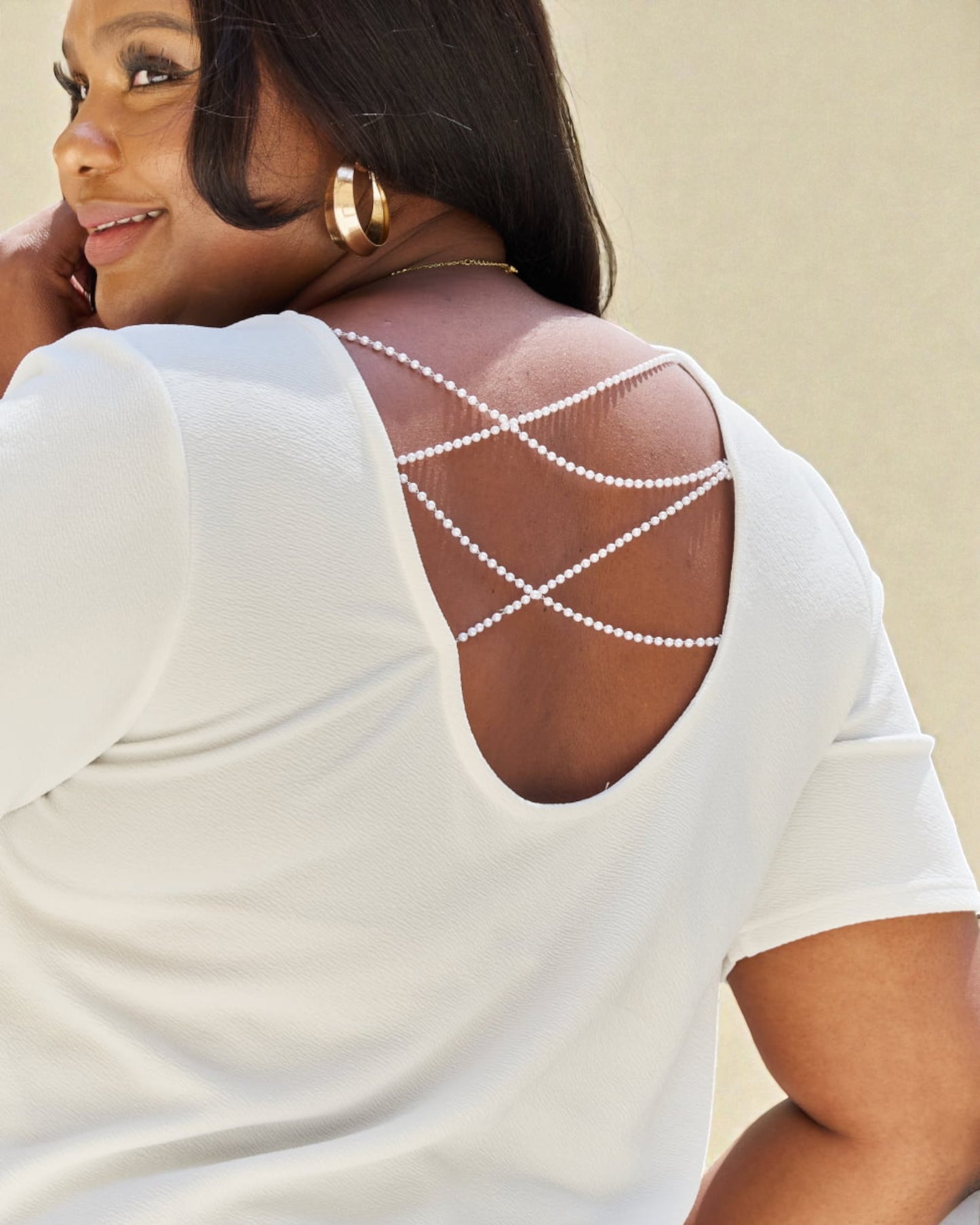 Woman wearing a white top with a unique back design on a beige background