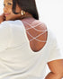 A close-up back view of a woman wearing a white short-sleeve top with decorative beaded crisscross straps across the open back, set against a bright white background.
