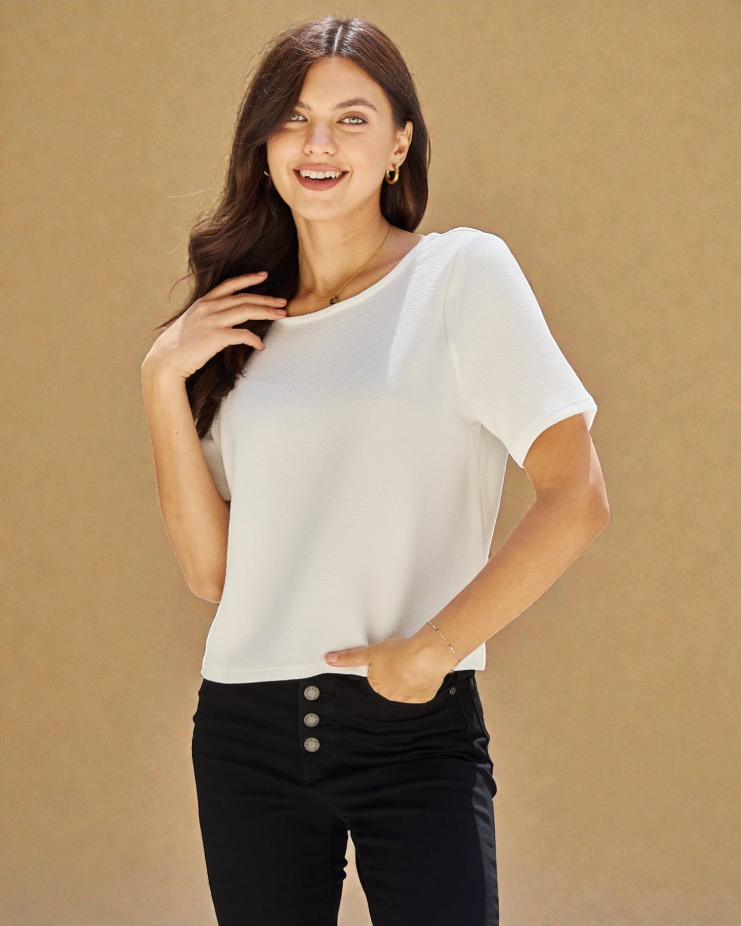 Woman wearing a white blouse and black pants against a beige background