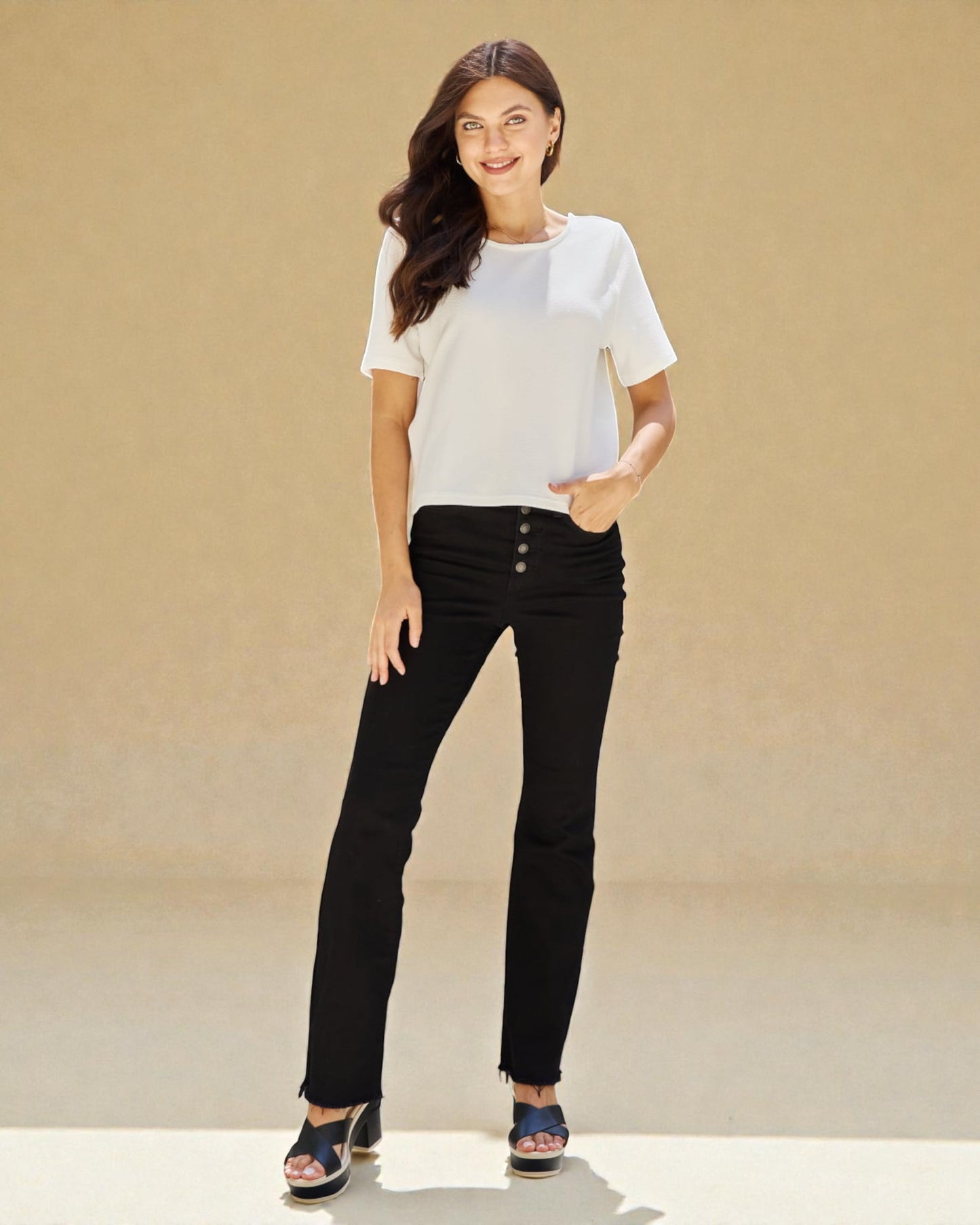 Woman wearing a white top and black pants against a beige background