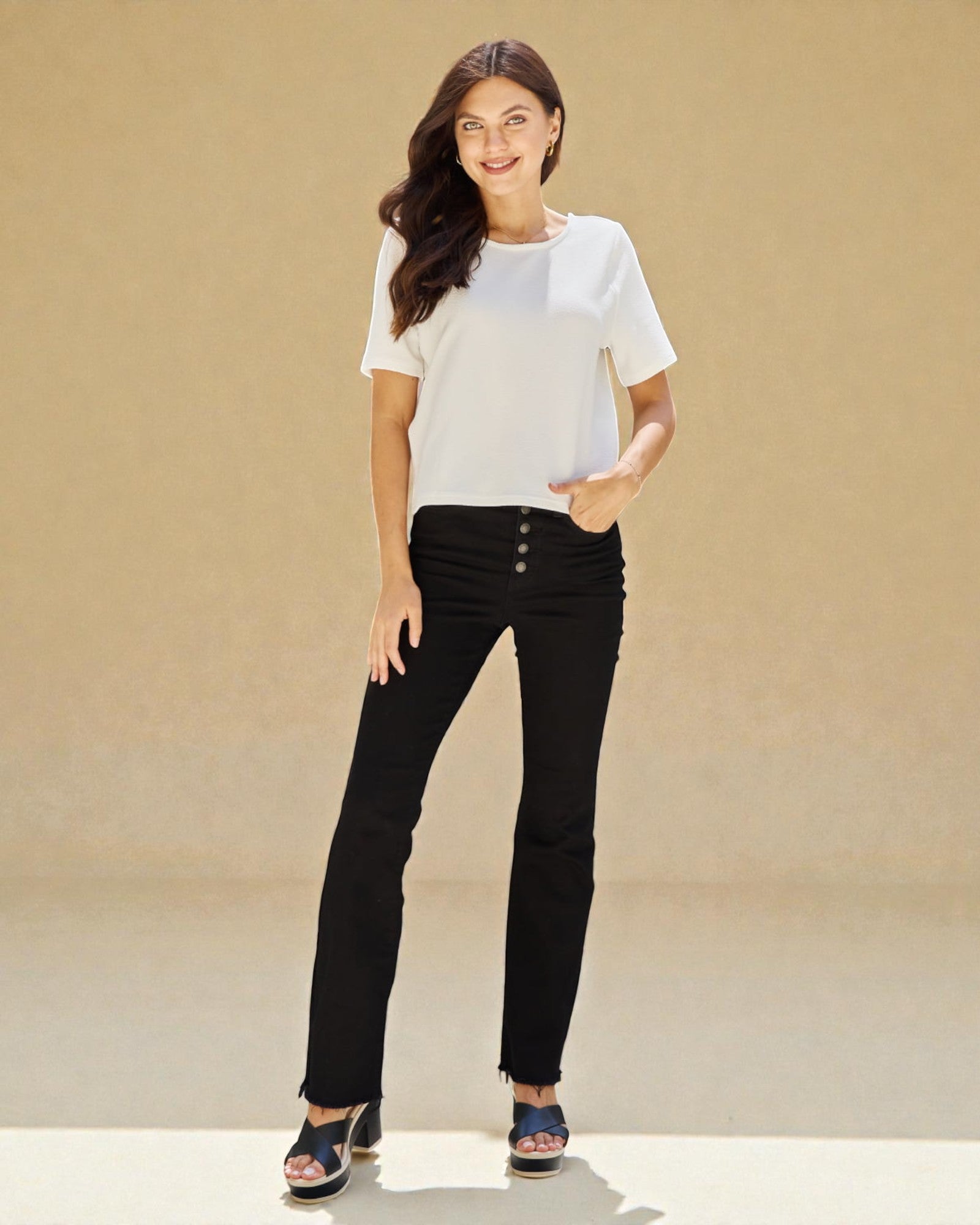 Woman wearing a white top and black pants against a beige background