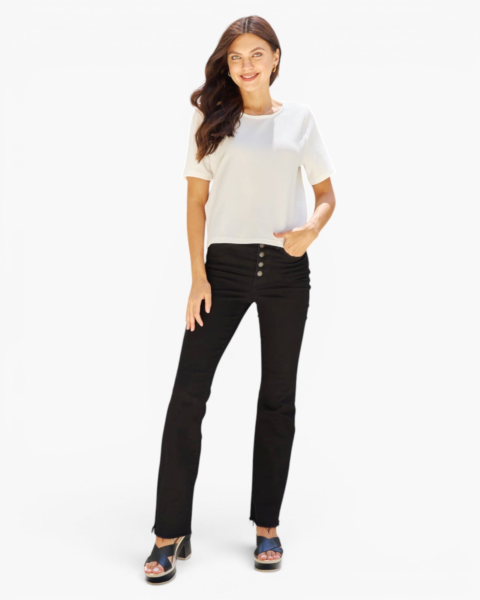A woman modeling a white short-sleeve top and black high-waisted straight-leg jeans with front buttons, paired with black sandals, against a plain white studio background.