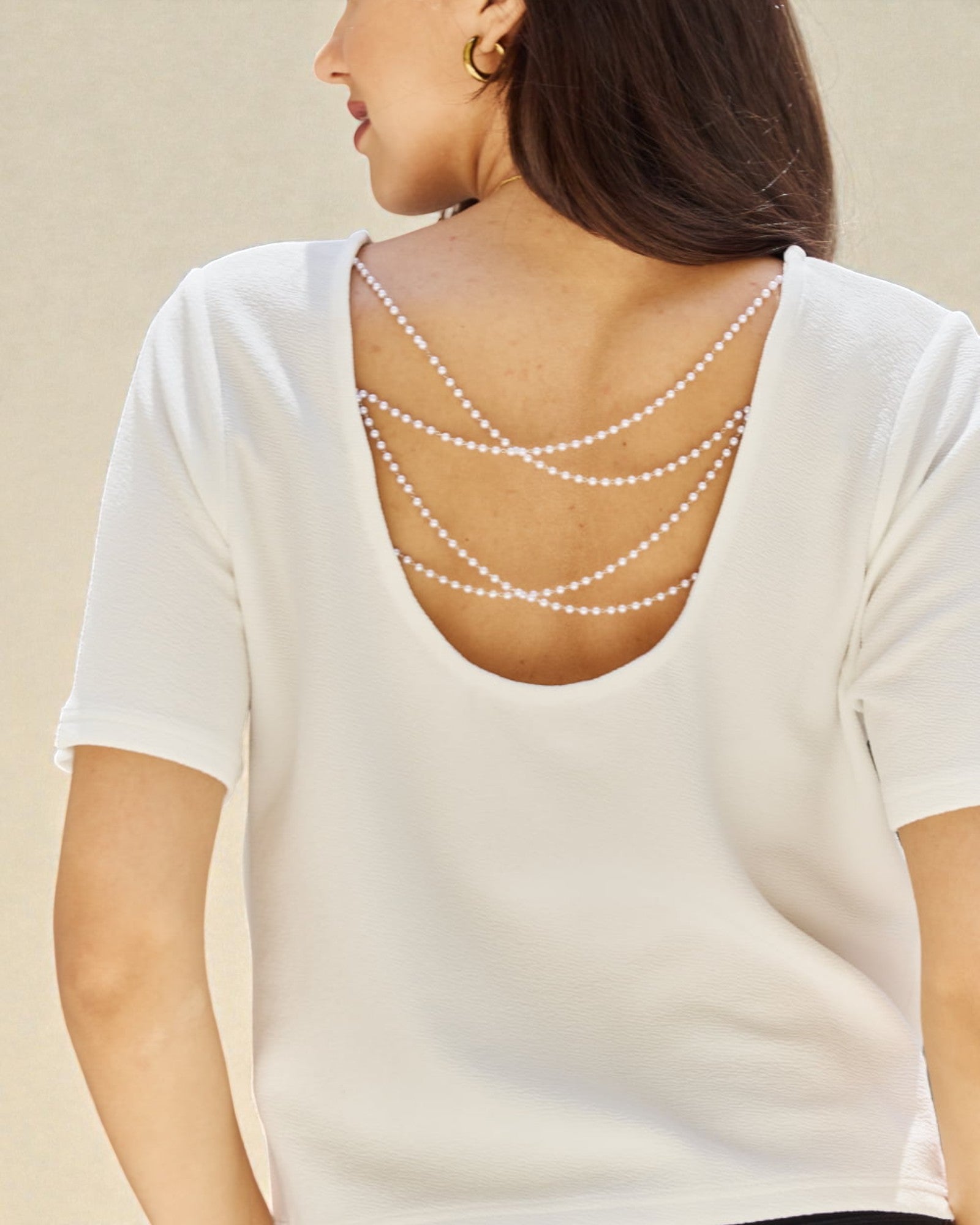White top with pearl embellishments on the back against a beige background