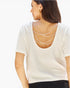 A woman shown from the back wearing a white short-sleeve top with three draped strands of pearl-like necklaces across the open back, paired with black bottoms against a plain white background.