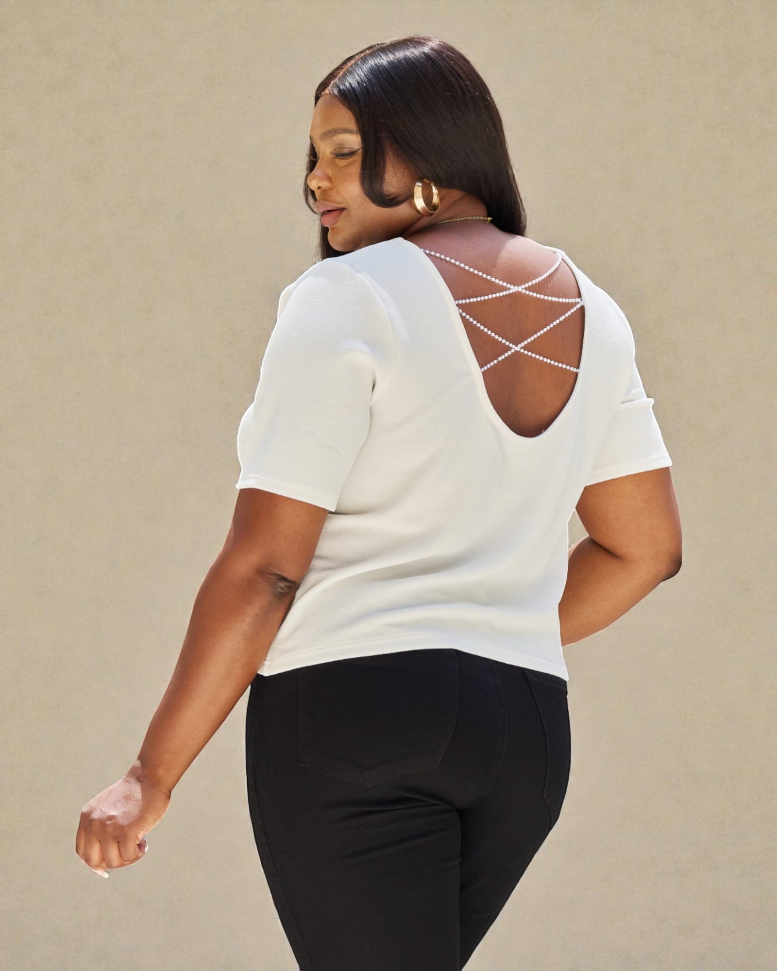 Woman wearing a white top with criss-cross back design on a beige background