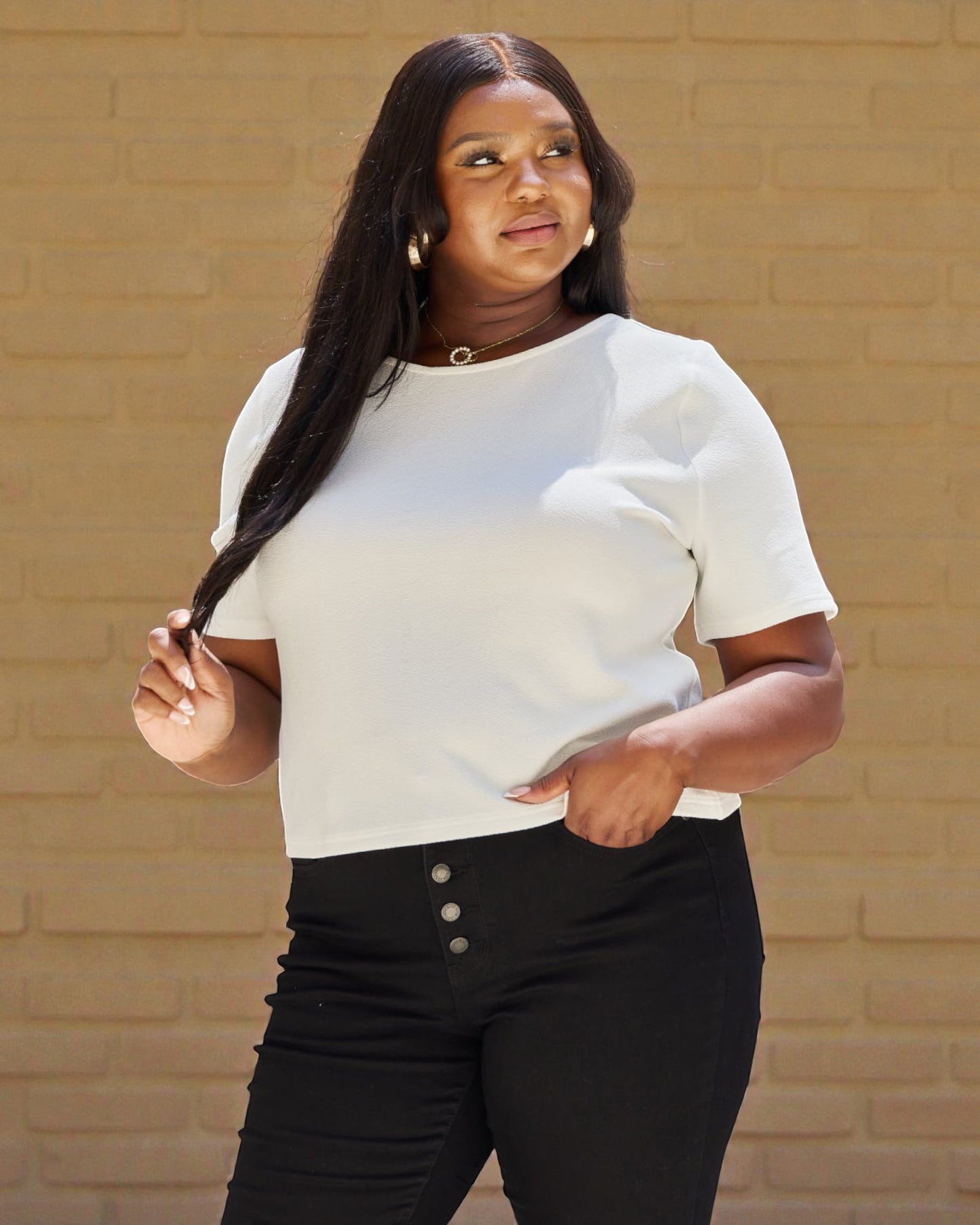 Woman wearing a white blouse and black pants against a beige brick wall