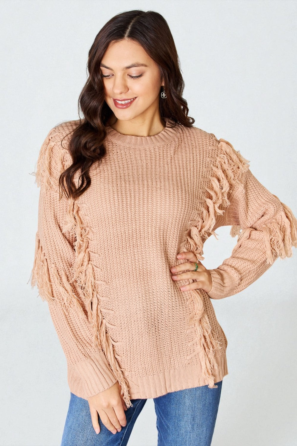 Woman wearing a beige knitted sweater with ruffled sleeves on a light gray background