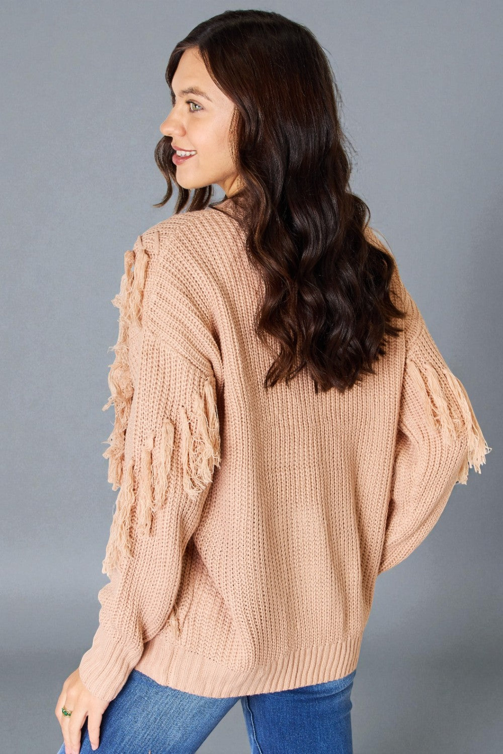 Woman wearing a beige knitted sweater with ruffled sleeves on a gray background