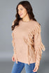 Woman wearing a beige fringed sweater against a gray background