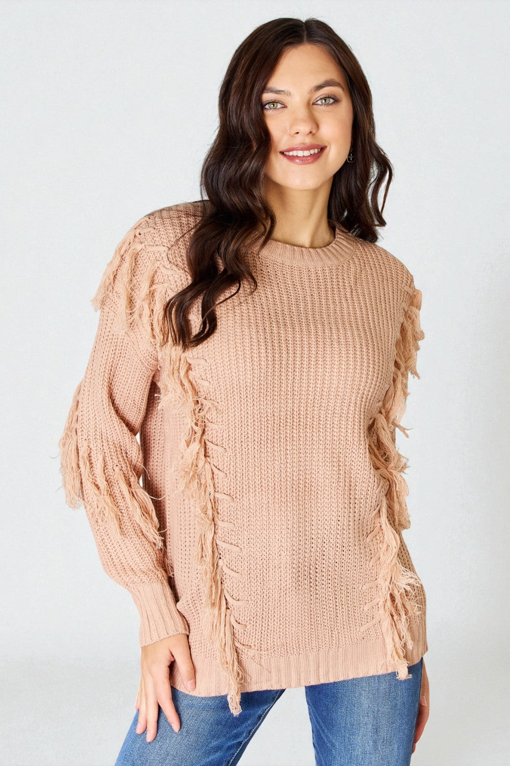 Woman wearing a beige knitted sweater with fringe details on a white background
