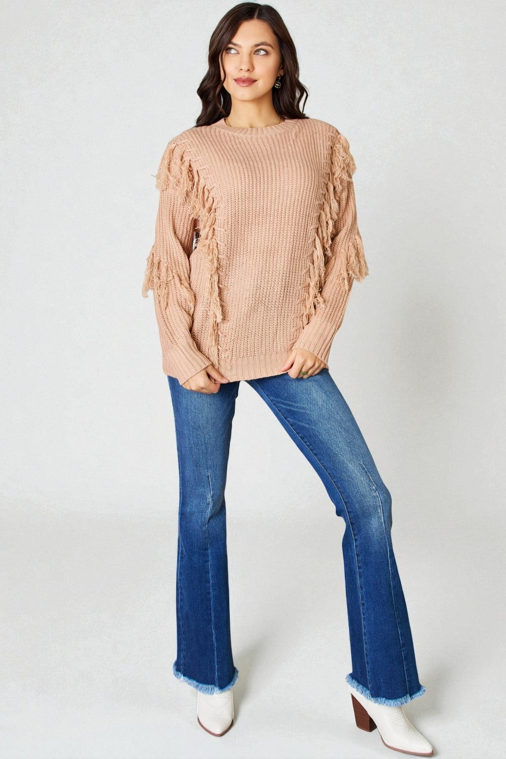Woman wearing a beige sweater and blue jeans on a white background