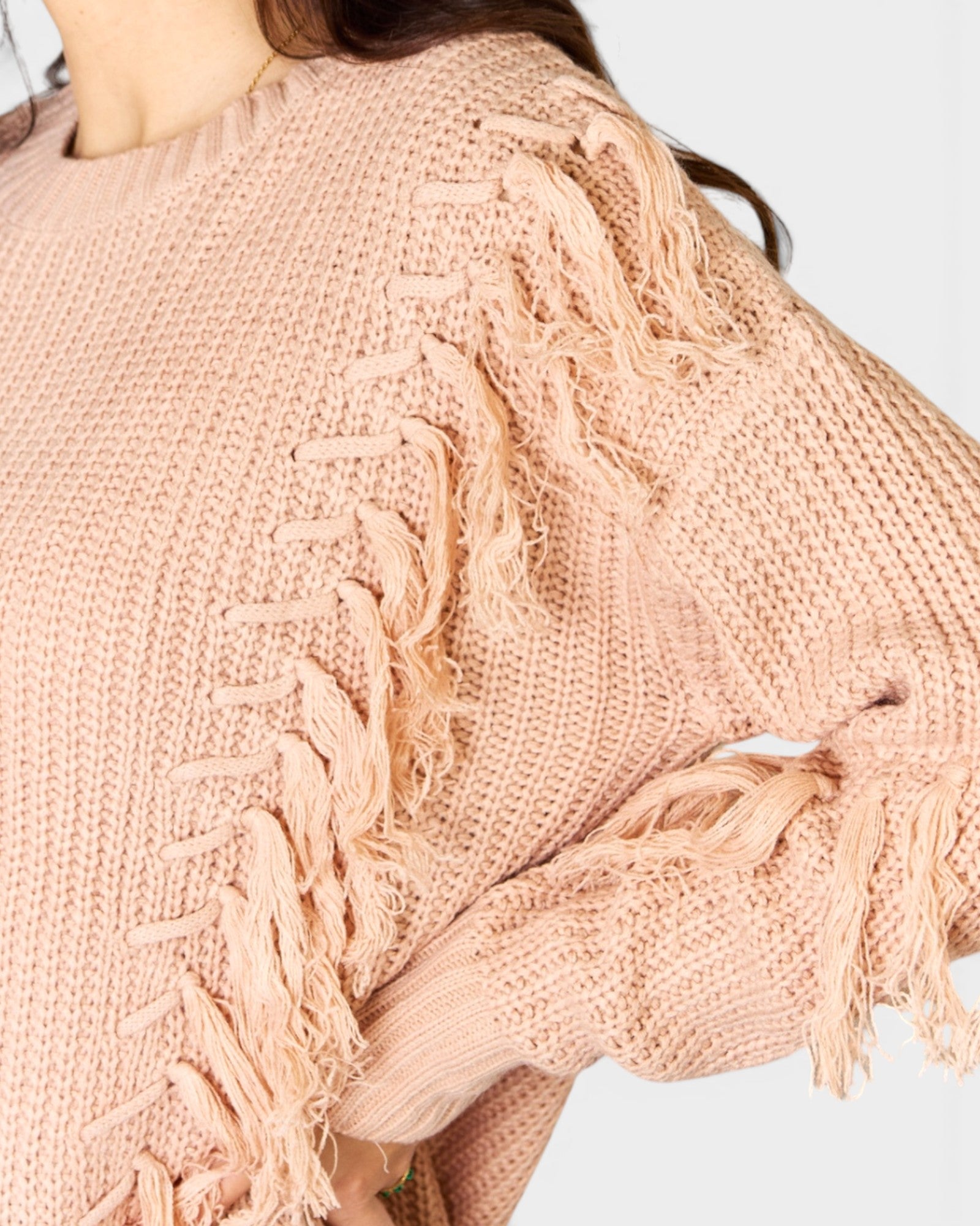 Close-up of a pink knitted cardigan with fringe details on a white background