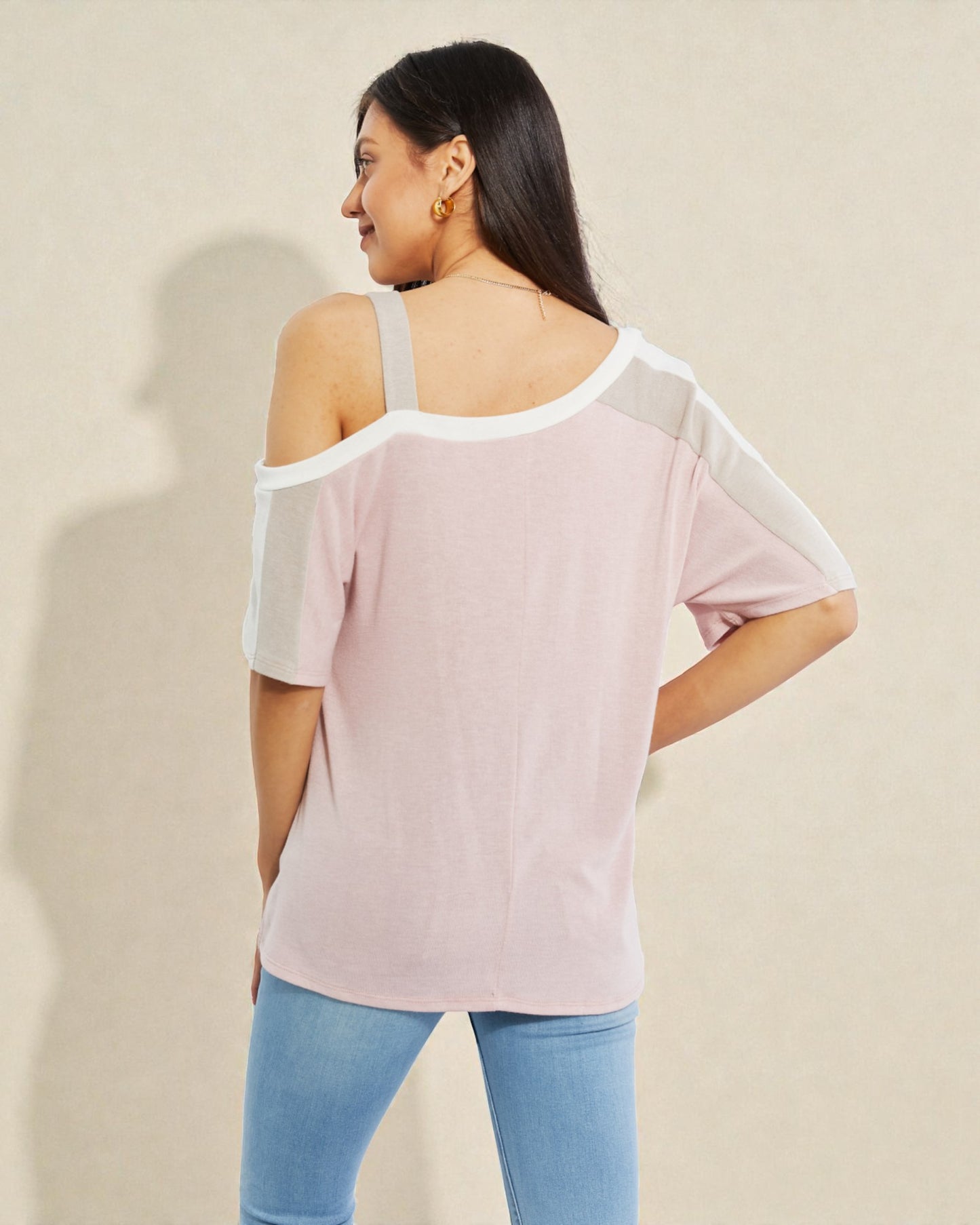 Woman wearing a light pink off-shoulder top with sheer sleeves against a beige background