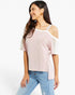 A woman wearing a light pink cold-shoulder top with white trim and sheer white sleeves, paired with light blue jeans, against a plain white background.