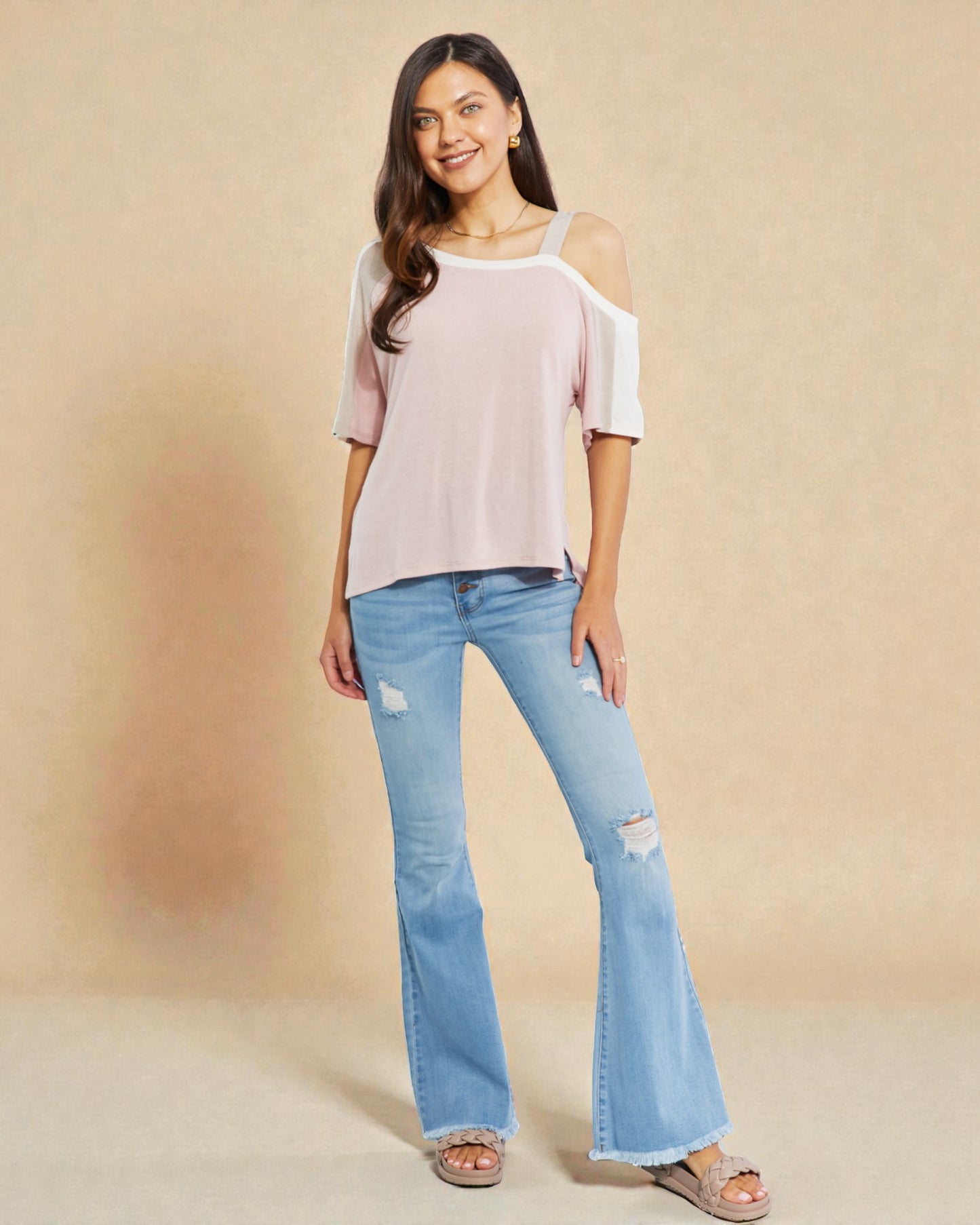 Woman wearing a light pink off-shoulder top and light blue flared jeans on a beige background