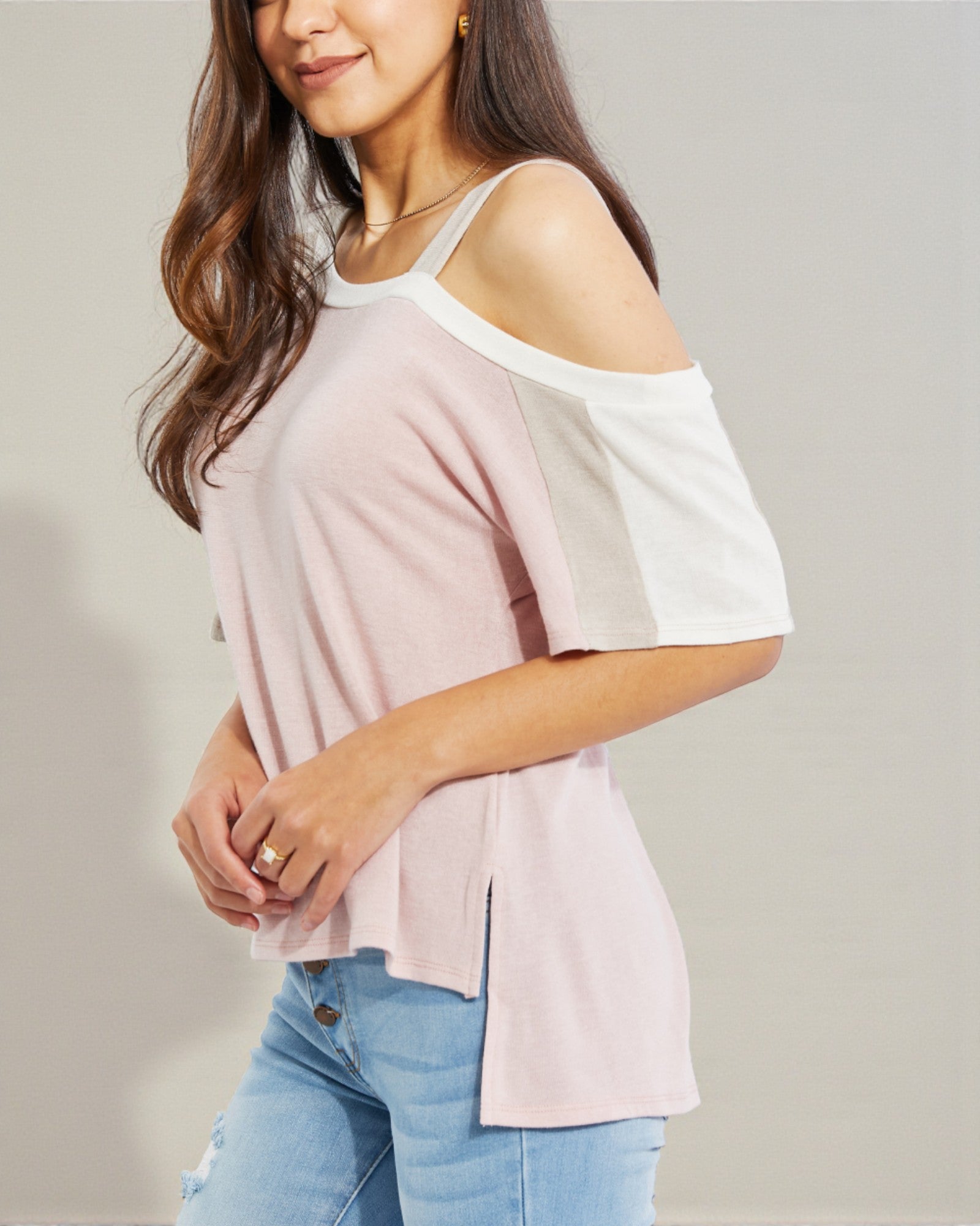Woman wearing a light pink off-shoulder top and blue jeans on a plain background