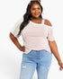 A woman modeling a light pink cold-shoulder t-shirt with sheer white raglan sleeves and light blue jeans, photographed against a solid white background.