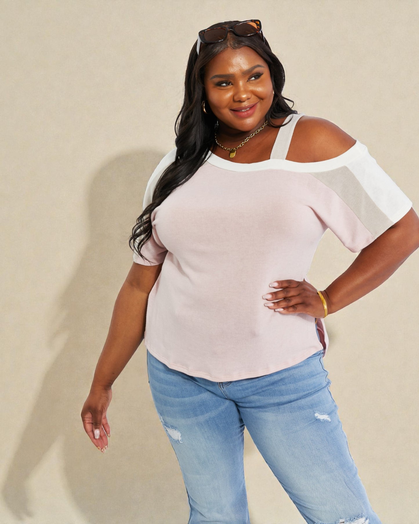 Woman wearing a light pink off-shoulder top and blue jeans against a beige background