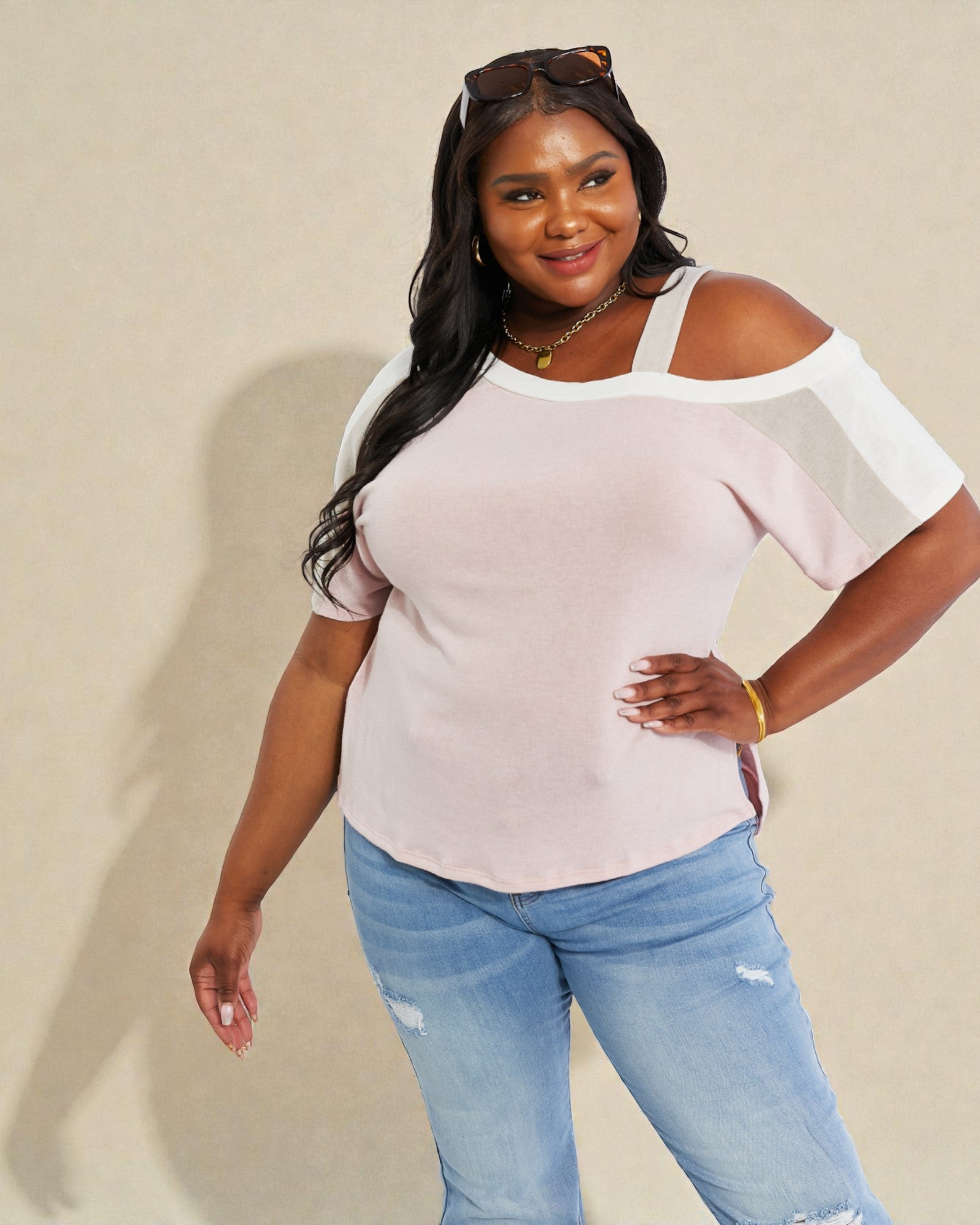 Woman wearing a light pink off-shoulder top and blue jeans against a beige background
