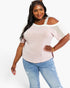 A woman modeling a pale pink cold-shoulder knit top with white mesh side panels and light blue distressed jeans against a plain white studio background.