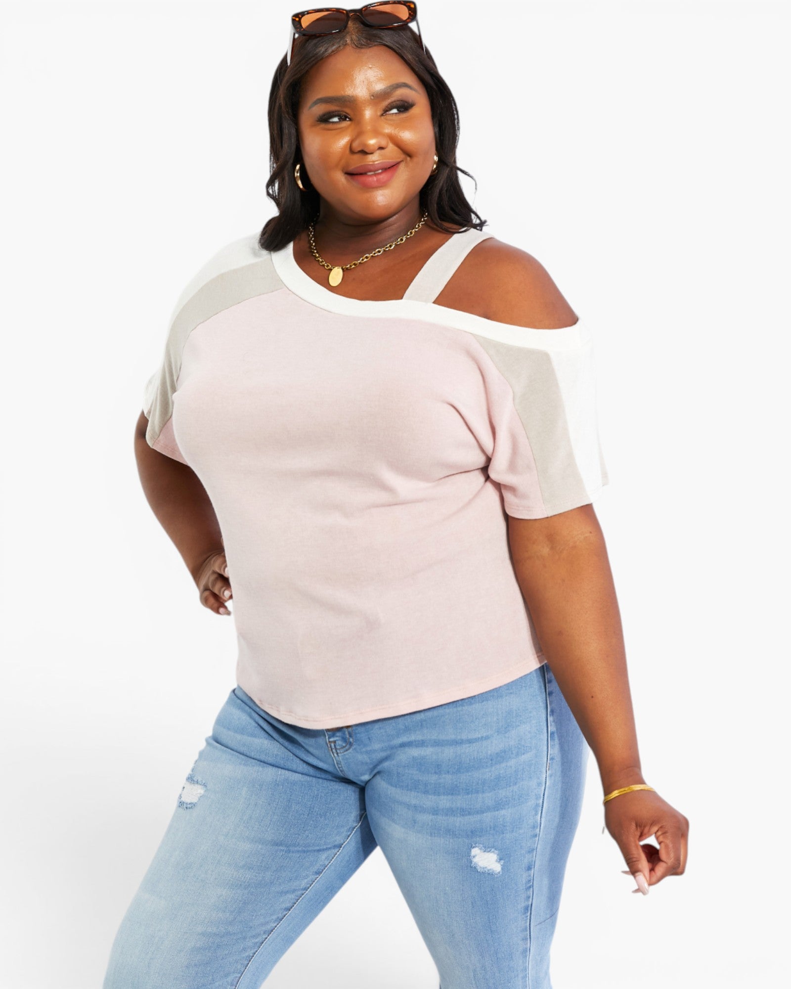 A woman modeling a short-sleeve knit top with a pale pink body, white shoulder yokes, and sheer white cold-shoulder sleeves, paired with light blue jeans against a plain white studio background.