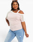A woman modeling a short-sleeve knit top with a pale pink body, white shoulder yokes, and sheer white cold-shoulder sleeves, paired with light blue jeans against a plain white studio background.