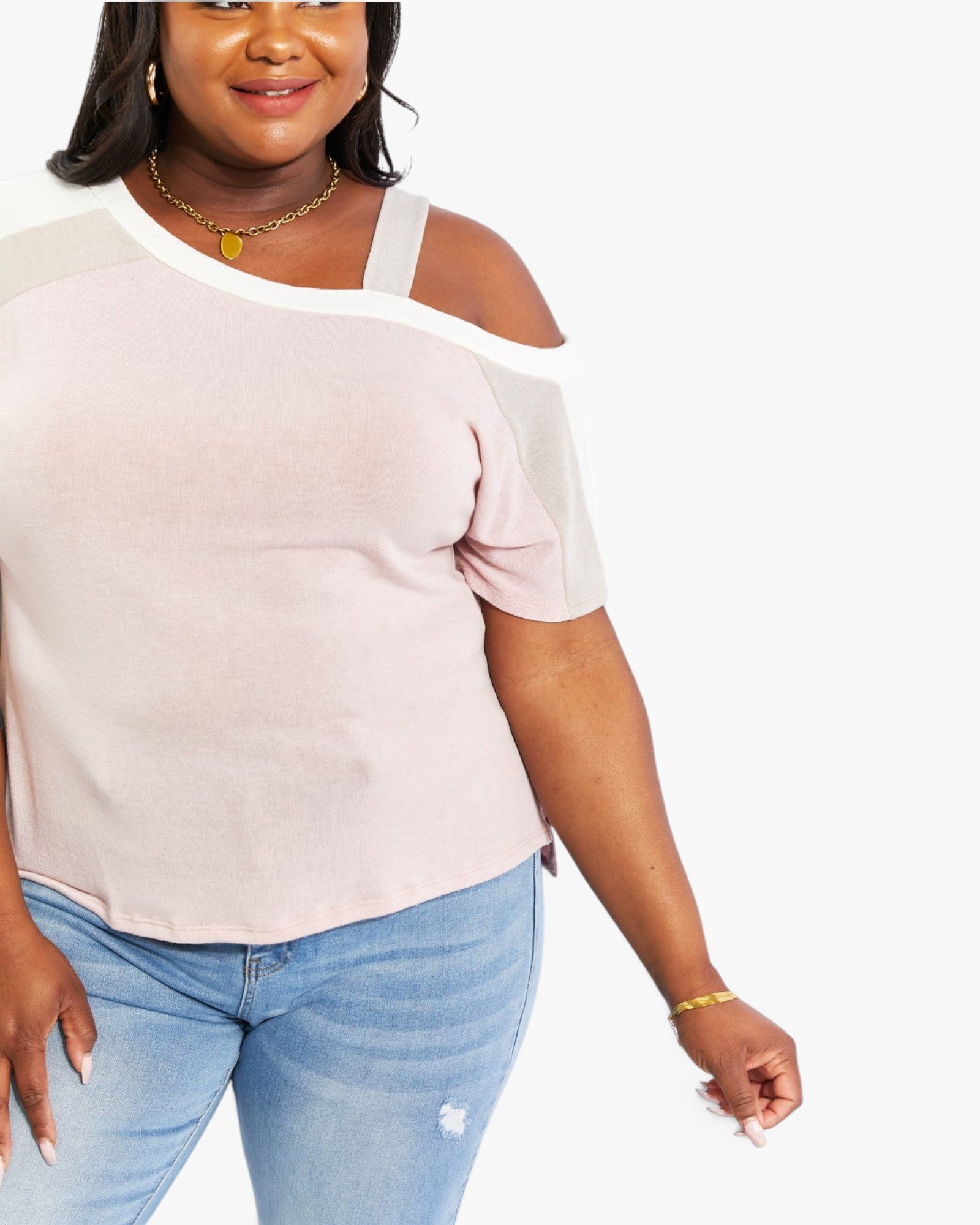 A plus-size woman wearing a pale pink cold-shoulder top with white trim and light blue jeans, shown against a plain white background.