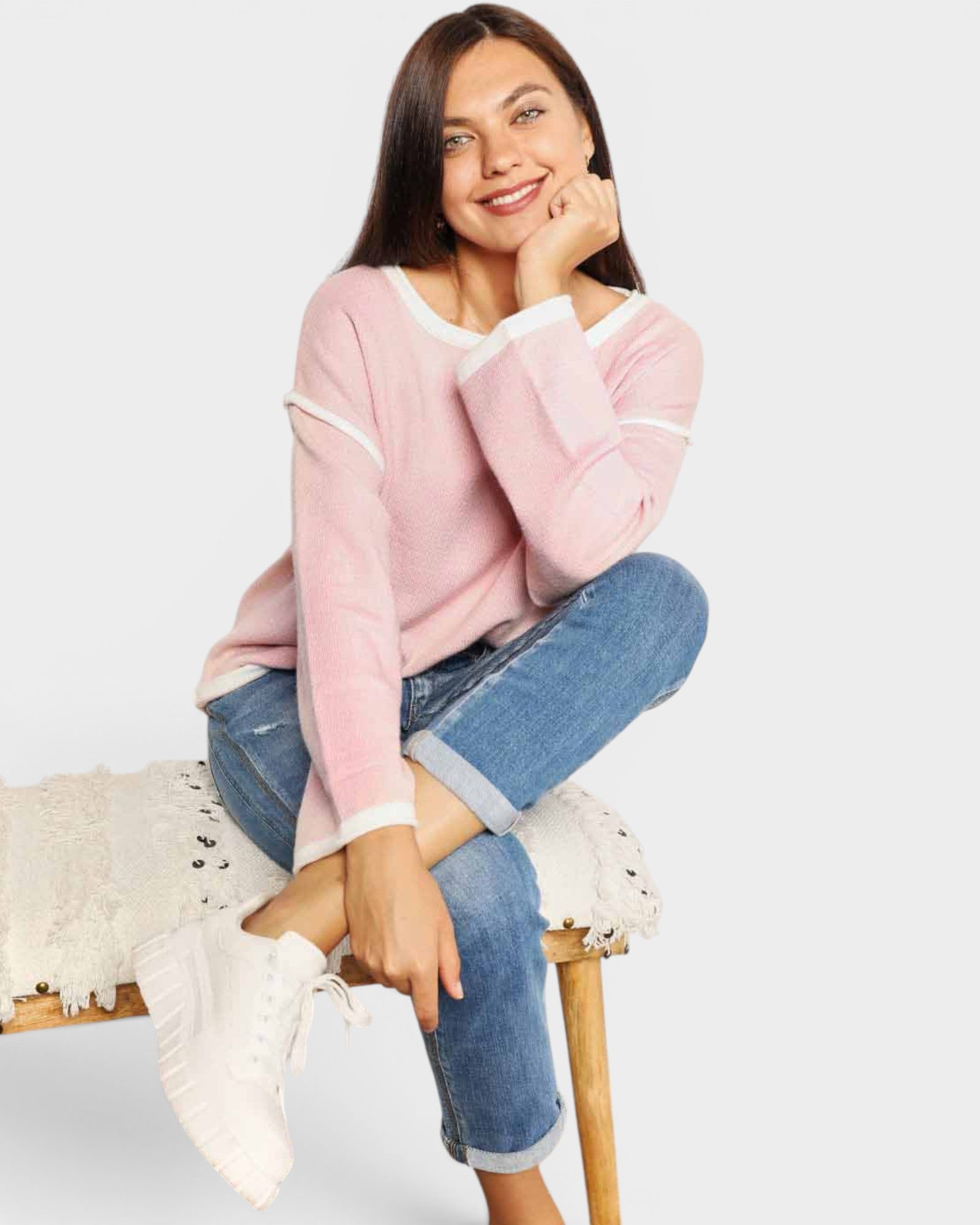 Woman wearing a pink sweater and blue jeans sitting on a white surface.