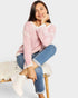 Woman wearing a pink sweater and blue jeans sitting on a white surface.