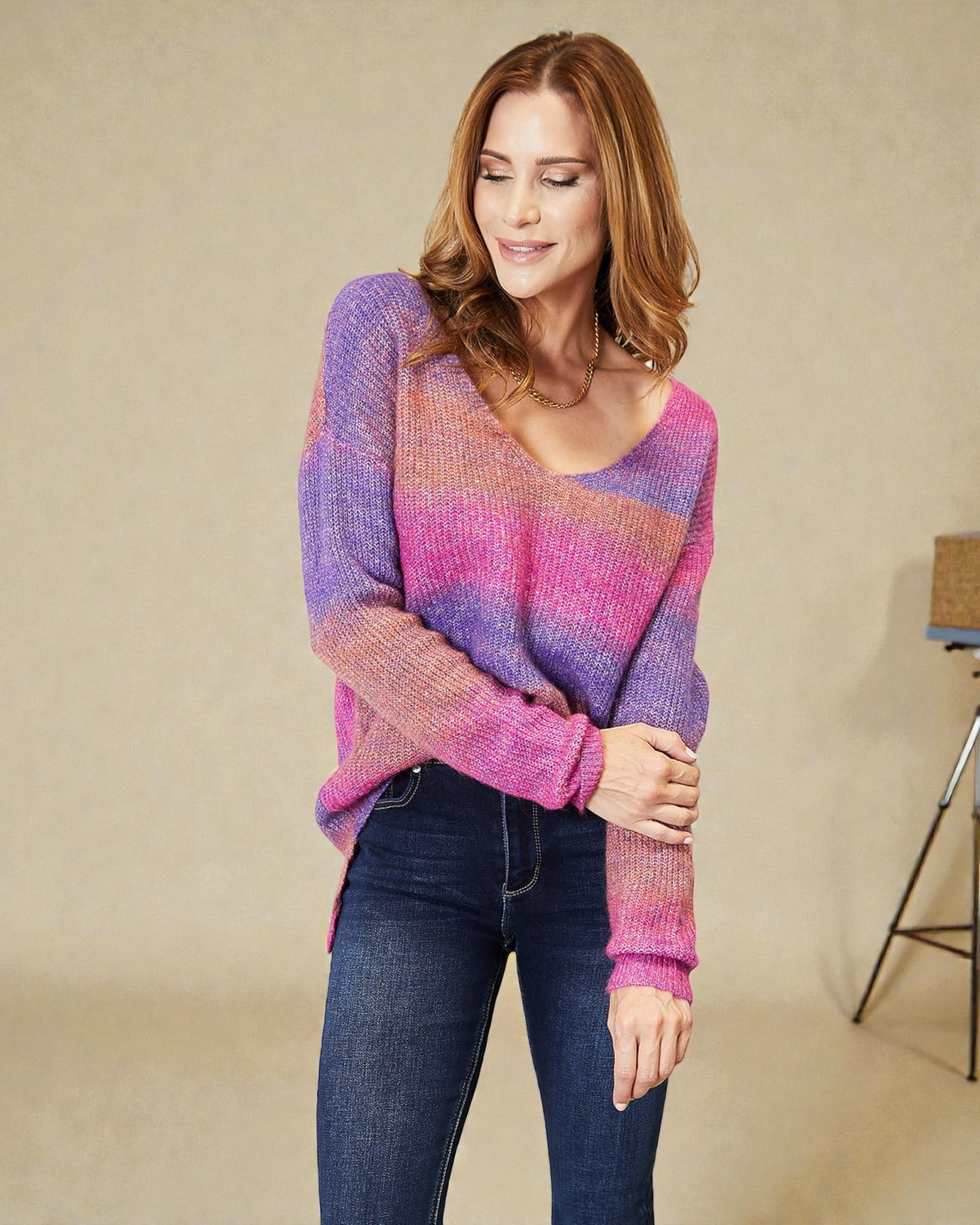 Woman wearing a colorful sweater and jeans against a beige background