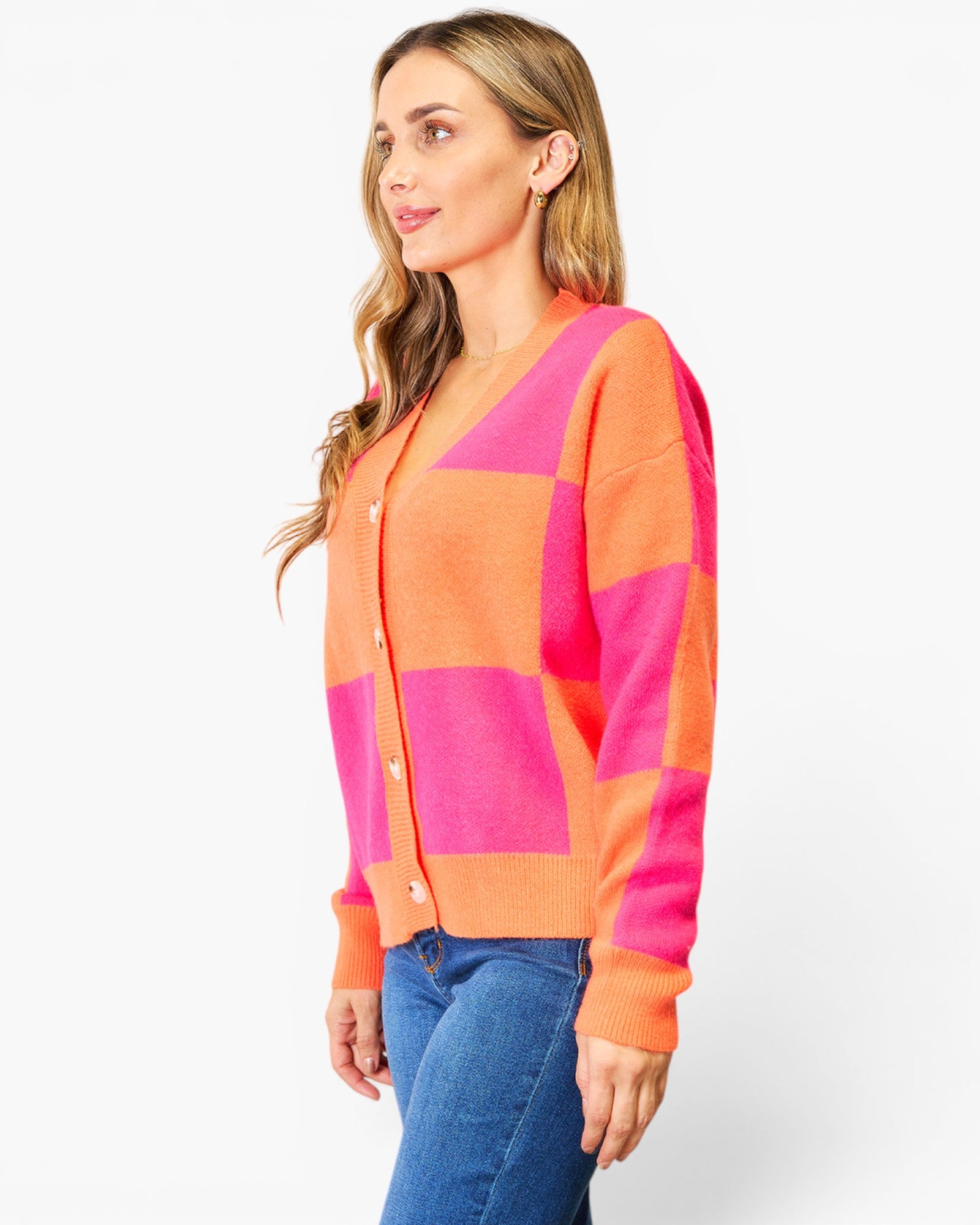 A woman wearing a bright orange and hot pink checkered cardigan sweater with blue jeans, photographed against a clean white studio background.