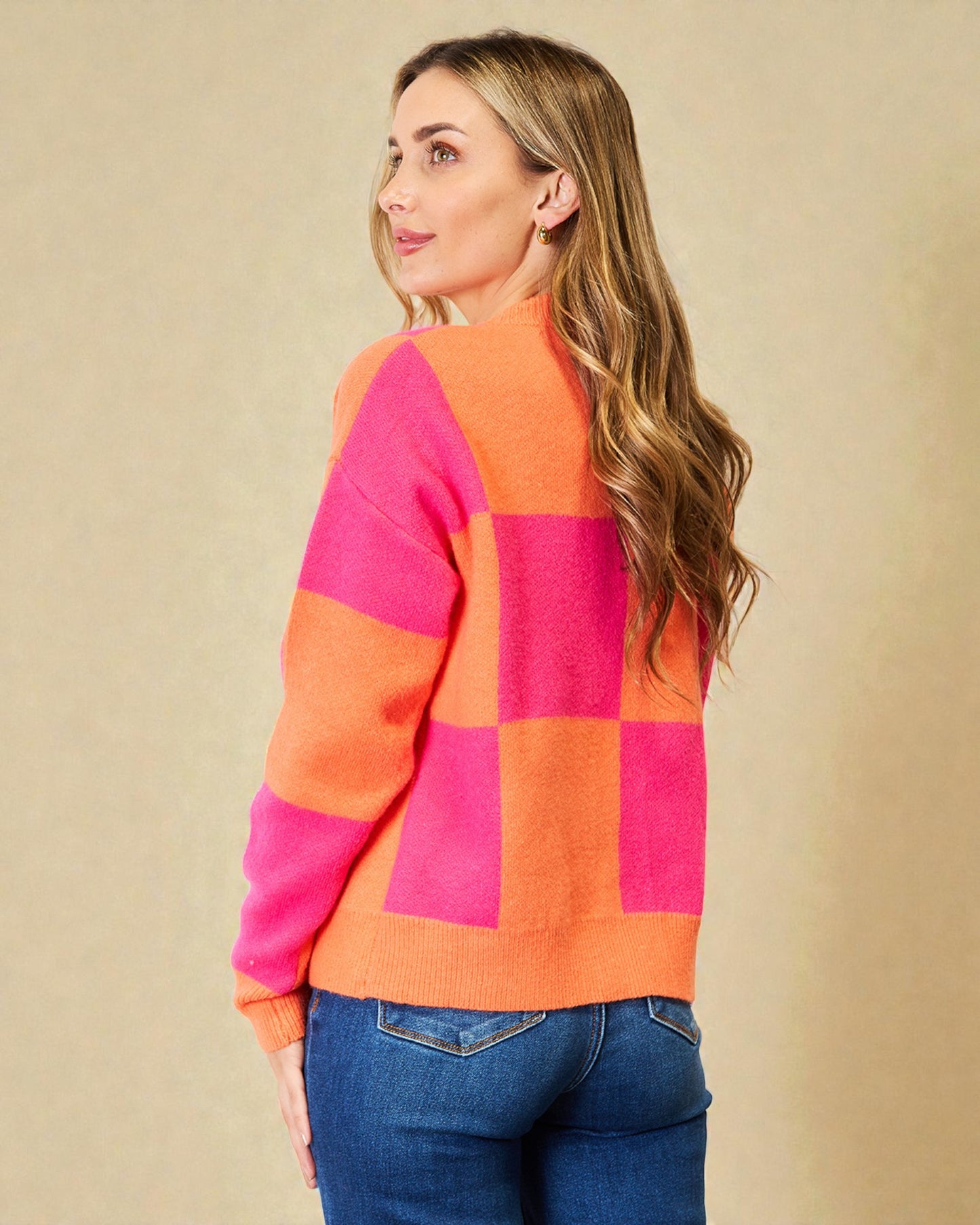 Woman wearing a colorful sweater with pink and orange squares on a beige background