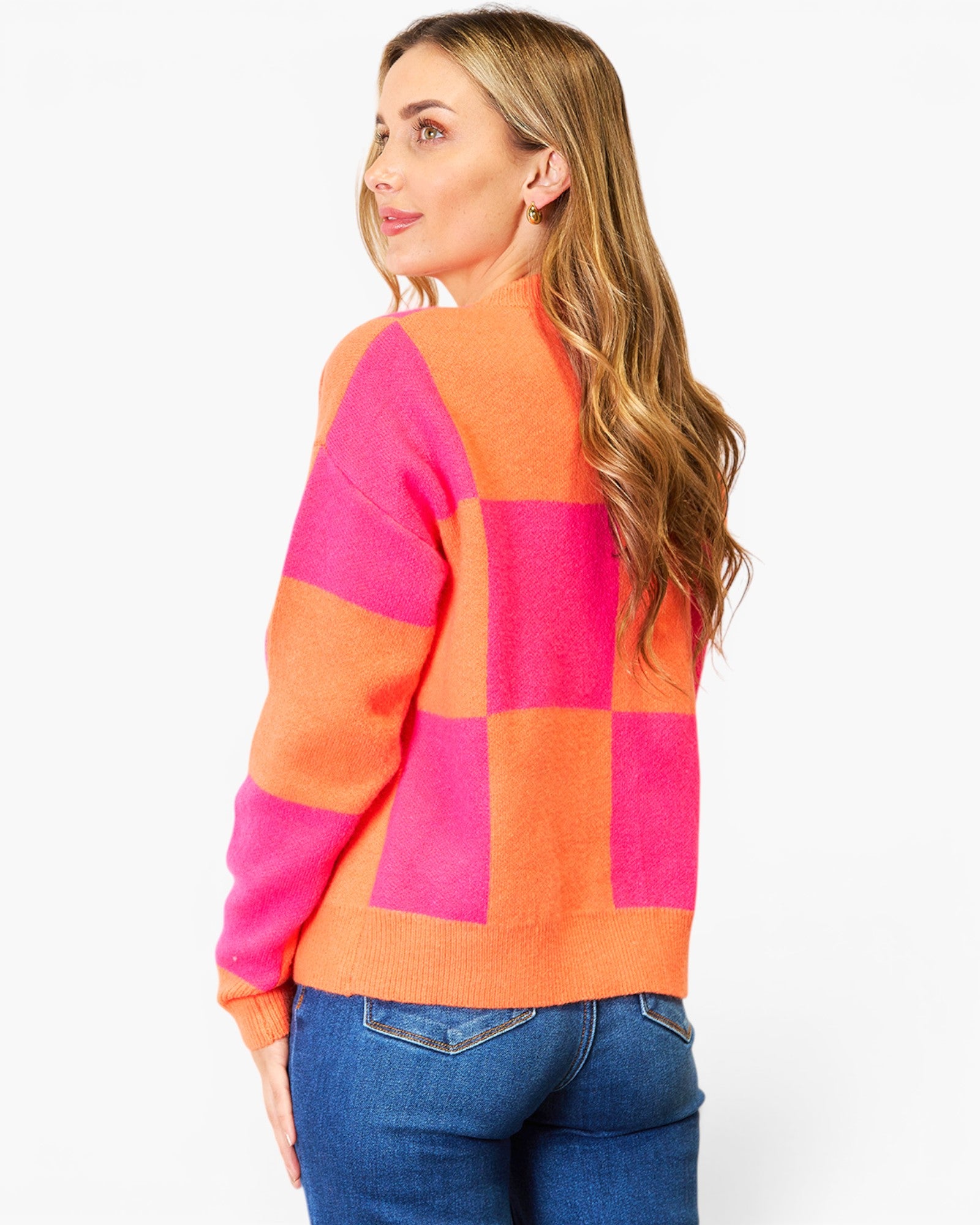 A woman wearing a bright orange and hot pink checkered knit sweater, shown from a three-quarters back view against a plain white background.