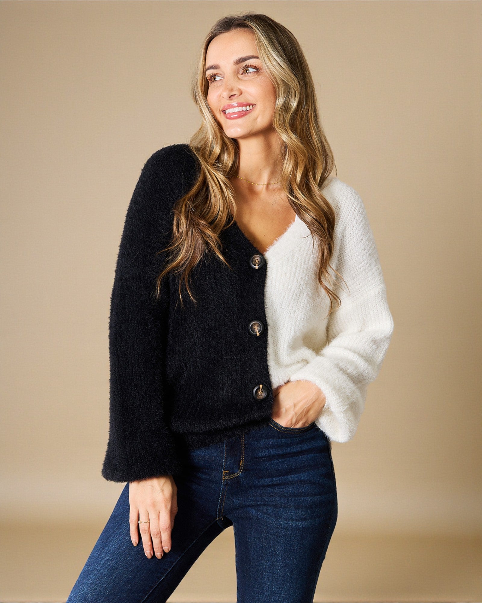 Woman wearing a black and white cardigan with blue jeans on a beige background
