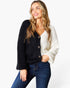 A woman modeling a fuzzy, color-block cardigan with a black left side and a white right side, paired with dark blue jeans against a plain white background.