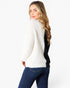 A woman wearing a fuzzy knit sweater with a color-block design in off-white and black, paired with dark blue jeans, photographed against a plain white studio background.