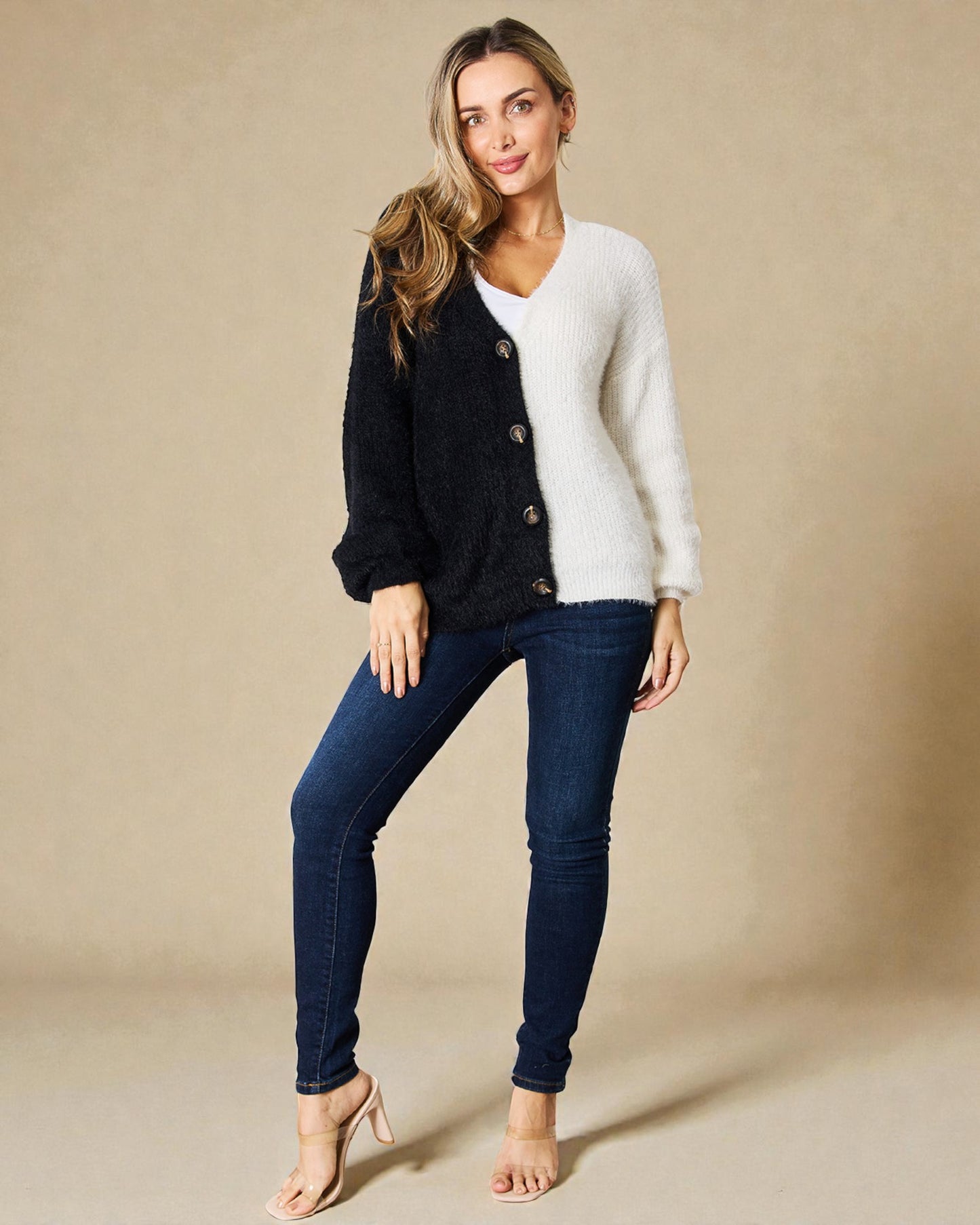 Woman wearing a black cardigan over a white shirt with blue jeans on a beige background